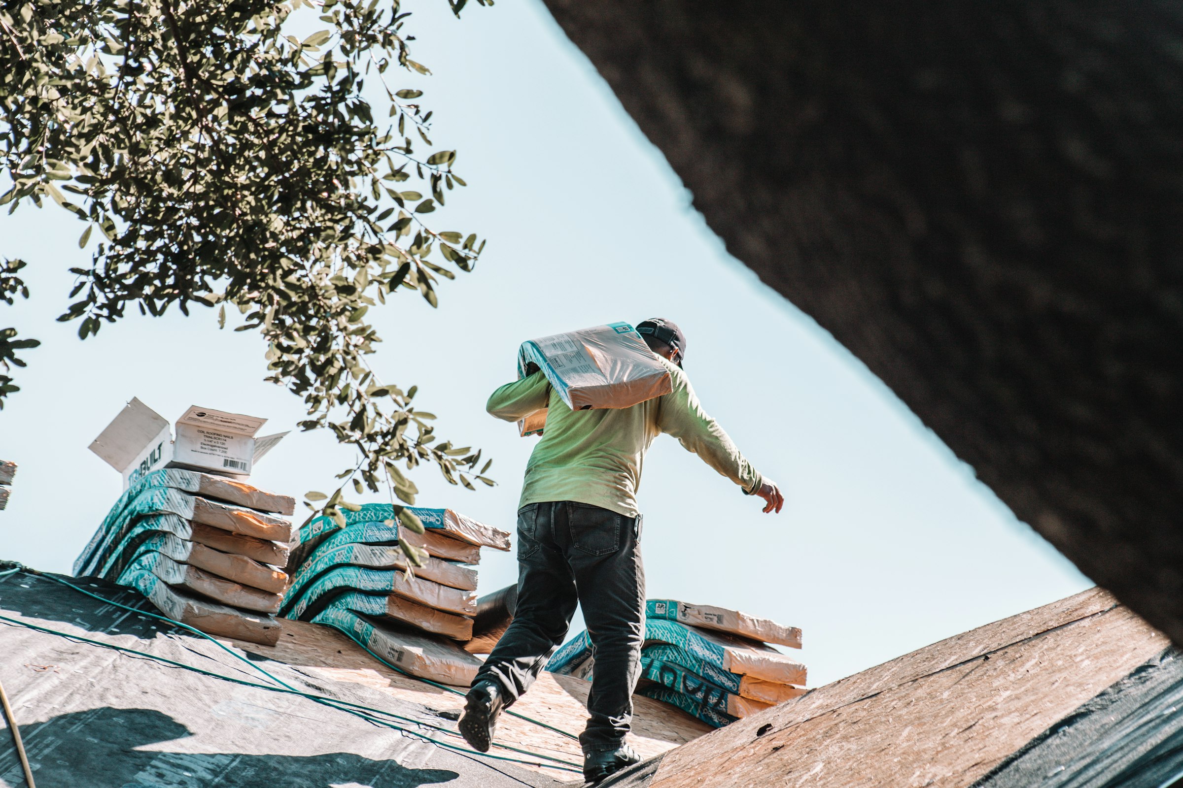 A roofer carrying a bundle of shingles across a residential roof